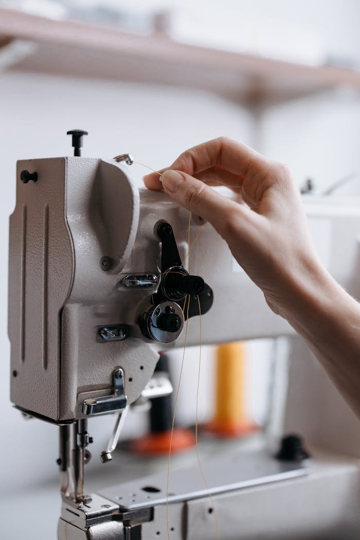 Close-up of a hand threading a sewing machine, highlighting precision and craftsmanship.