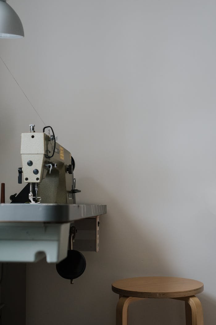 A sewing machine and stool in a modern, minimalist workspace with soft lighting.