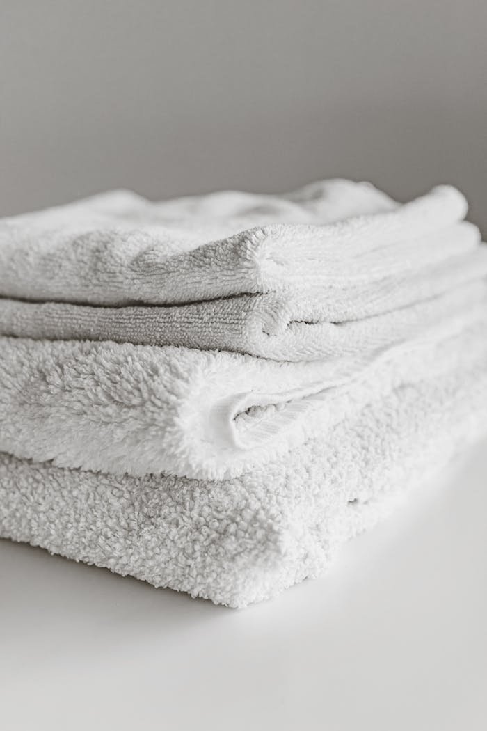 Neatly folded clean white towels stacked on a surface, perfect for home or spa use.